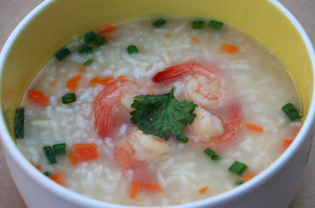 Rice congee mixed with shrimp in the round bowl on the brown floor. Sprinkled with spring onions and...