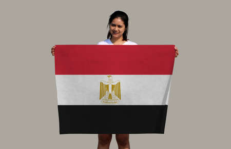 Pretty lady is holding Egypt flag in her hands on grey background.の写真素材