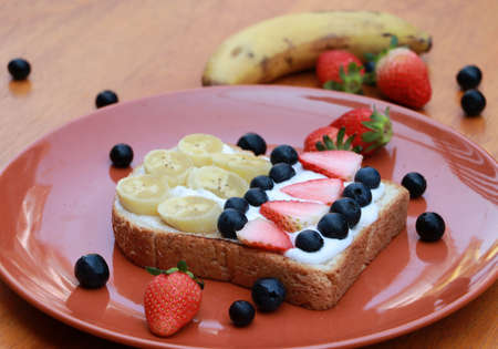 Breakfast in the orange color of round plate on the wooden floor. Slice of bread with whipped cream and fruit, Strawberry, Blueberry and Banana.の写真素材