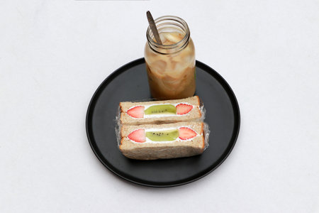 Breakfast in the black color of round plate on the white floor. Strawberry and kiwi fruit with cream...