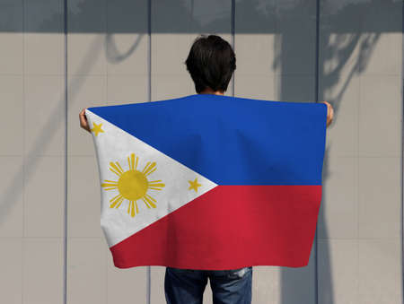 The man is holding Philippines flag on his shoulder and turn back on grey background.の写真素材