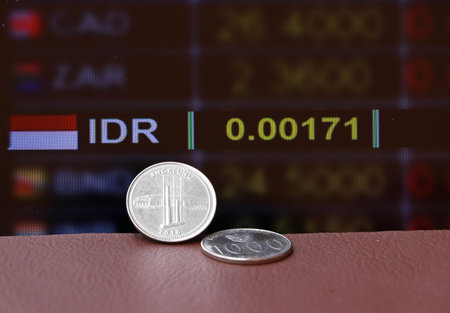 Two coins of one thousand Indonesia Rupiah money on brown floor with digital board of currency...