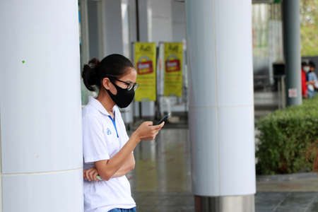 Nonthaburi, Thailand - 30 May, 2020 : Adolescent girls wearing glasses with  hygienic mask and stand using a mobile phone.のeditorial素材