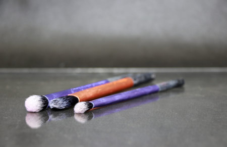 Makeup brush in purple and golden color handle lay on the floor with a reflection. They are pointed...