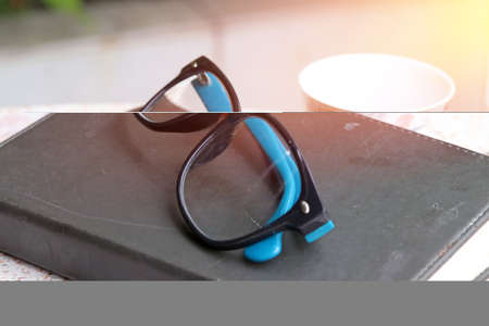 Black and blue glasses put on the book with tea cup on the table in the morning. the concept of...
