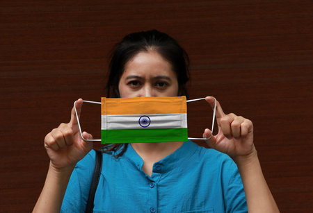 A woman with India flag on hygienic mask in her hand and lifted up the front face on brown...