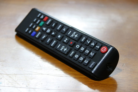 Black remote control isolated on wooden table. For control of a machine or apparatus from a distance by means of signals transmitted from a radio or electronic device.の写真素材