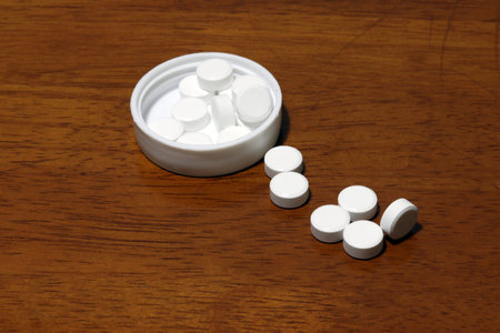 Pile of white round medicine on the wooden floor and white plastic cap. paracetamol can help to...