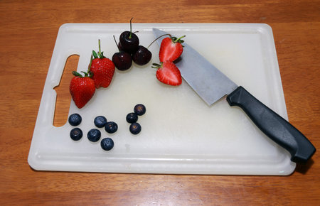 Cherry, berry fruit, strawberry and chopped strawberry with knife on the white chopping board on the...