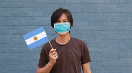Masked man in brown shirt and small Argentina flag in hand. Concept of protection and fighting COVID.の写真素材