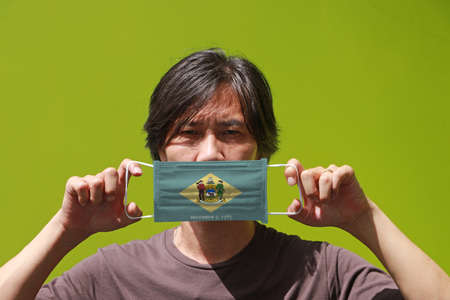 A man and hygienic mask with Delaware flag pattern in his hand and raises it to cover his face. A mask is a very good protection from Tiny Particle or virus corona or Covid 19.の写真素材