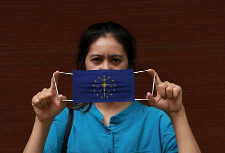 A woman and hygienic mask with Indiana flag pattern in her hand and raises it to cover her face. A mask is a very good protection from Tiny Particle or virus corona or Covid 19.の写真素材