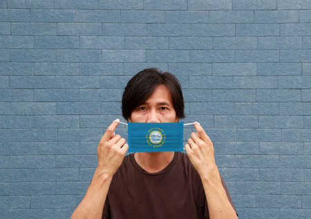 A man and hygienic mask with South Dakota flag pattern in his hand and raises it to cover his face. A mask is a very good protection from Tiny Particle or virus corona or Covid 19.の写真素材