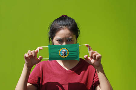 A woman and hygienic mask with Washington flag pattern in her hand and raises it to cover her face. A mask is a very good protection from Tiny Particle or virus corona or Covid 19.の写真素材