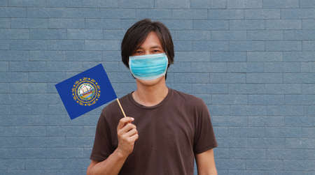 Masked man in brown shirt and New Hampshire flag in hand. Concept of protection and fighting COVID.の写真素材