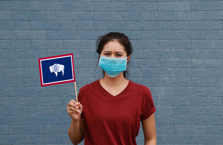 Masked woman in brown shirt and Wyoming flag in hand. Concept of protection and fighting COVID.の写真素材