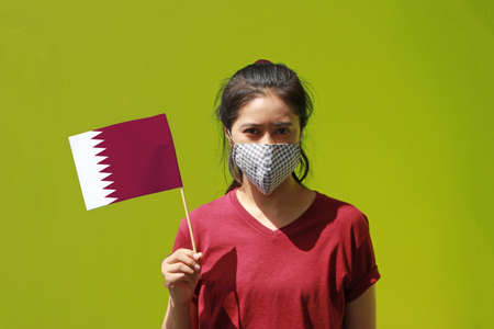 Masked woman in brown shirt and small Qatar flag in hand. Concept of protection and fighting COVID.の写真素材