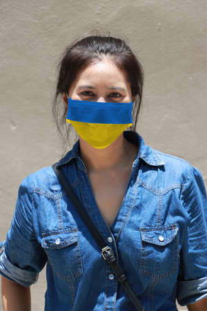 Ukraine flag on hygienic mask. Masked woman prevent germs and wear denim dress. Tiny Particle or virus corona protection. Concept of Combating illness.の写真素材