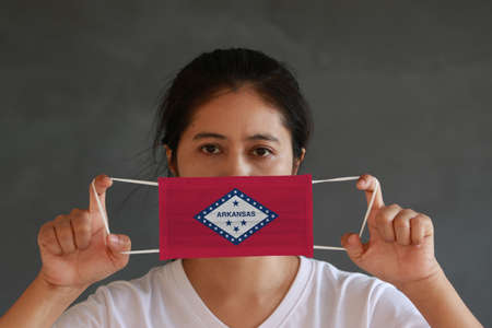 A woman and hygienic mask with Arkansas flag pattern in her hand and raises it to cover her face. A mask is a very good protection from Tiny Particle or virus corona or Covid 19.の写真素材