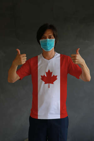 Man wearing hygienic mask and wearing Canadian flag colored shirt with thumbs up on both hands. Concept of protect tiny dust or disease of Canada.の写真素材