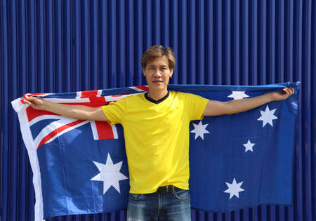 The man in yellow shirt is holding Australia flag on his shoulder on blue background.の写真素材