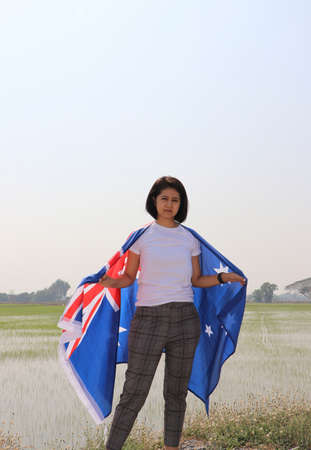 pretty lady in white shirt with Australia flag on her shoulder on nature view and rice fields background.の写真素材