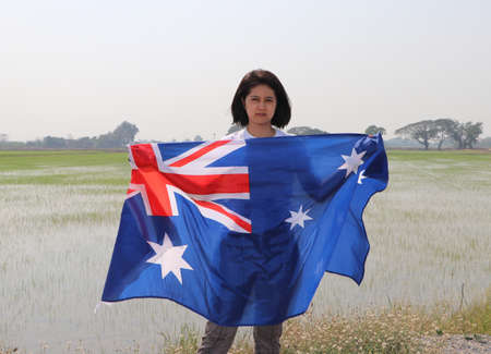pretty lady is holding Australia fabric flag in her hands nature view and rice fields background.の写真素材