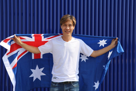 The man in white shirt is holding Australia flag on his shoulder on blue background.の写真素材