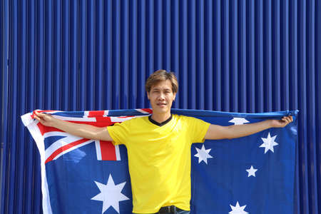 The man in yellow shirt is holding Australia flag on his shoulder on blue background.の写真素材