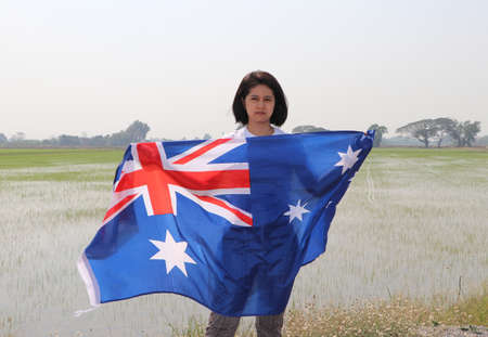 pretty lady is holding Australia fabric flag in her hands nature view and rice fields background.の写真素材