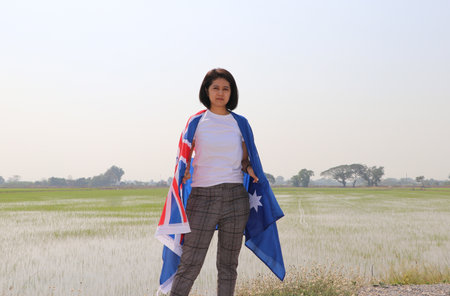 pretty lady in white shirt with Australia flag on her shoulder on nature view and rice fields background.の写真素材