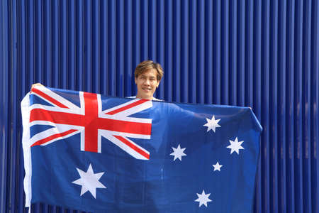 The man is holding Australia fabric flag in his hands on blue background.の写真素材