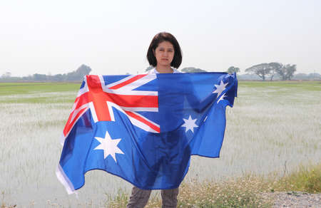 pretty lady is holding Australia fabric flag in her hands nature view and rice fields background.の写真素材