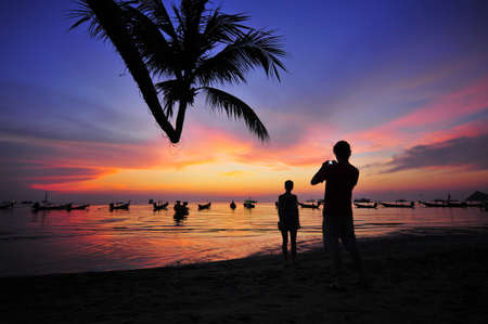 Silhouette picture about man taking pictures of woman at the beach on sunset.の写真素材