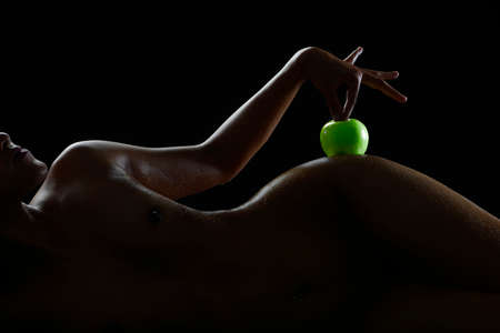 Naked woman sexy body silhouette pose like nude abstract by hold an apple on her hip on black background.の写真素材