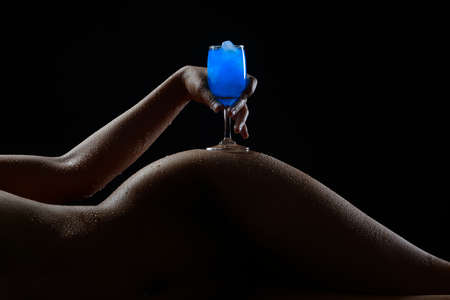 Naked woman sexy body silhouette pose like nude abstract by hold blue glass on her hip on black background.の写真素材