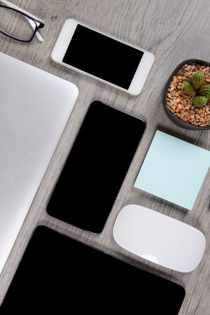Office table with laptop computer, digital tablet, pen, smartphone, mouse, eyeglasses and coffee on...