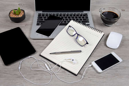 Office table with laptop computer, notebook, digital tablet, pen, smartphone, mouse, eyeglasses and coffee on white wood background. Desktop office mockup concept.の写真素材