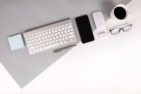 Flat lay photo of Office table with keyboard, notebook, digital tablet, mobile phone, Pencil, eyeglasses  on modern two tone (white and grey) background. Desktop office mockup concept.の写真素材