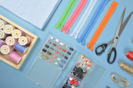Flat lay of sewing material contains the fabrics, scissors, shirt buttons, zipper, pin and colorful...