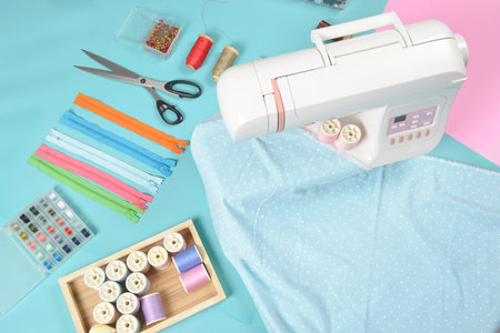 Fabrics on sewing machine amid the scissors, shirt buttons, zipper, pin and colorful thread rolls...