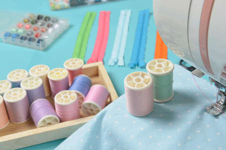 Fabrics on sewing machine amid the scissors, shirt buttons, zipper, pin and colorful thread rolls for sewing on blue background, Sewing and needlework concept.の写真素材