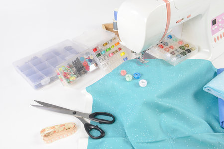 Sewing machine and colorful thread rolls, scissors, fabric and accessories for sewing on white...