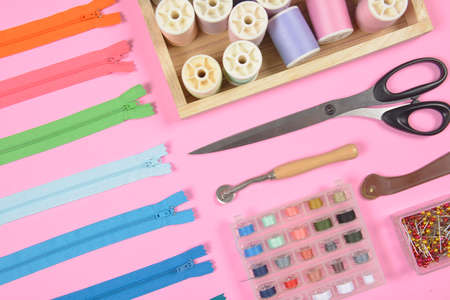 Flat lay of sewing material contains the scissors, measuring tape, zipper, pin and colorful thread rolls for sewing on pink background, Sewing and needlework concept.の写真素材