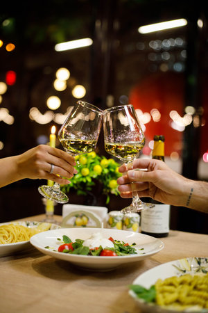Close up of two hands holding glasses of white wine on table in restaurantの写真素材