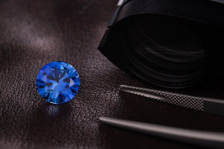 Blue sapphire jewel stone on a black leather background with tweezersの素材