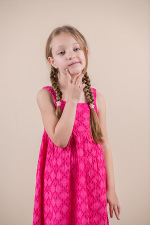 Portrait of a cute little girl in a pink dress on a beige backgroundの写真素材