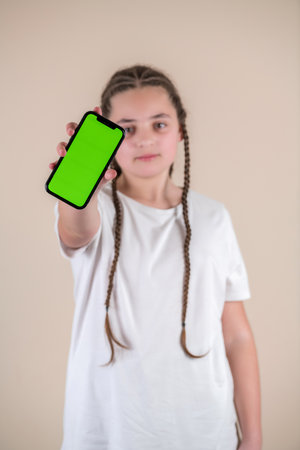 Teenage girl showing smartphone with green screen, isolated on beige backgroundの写真素材