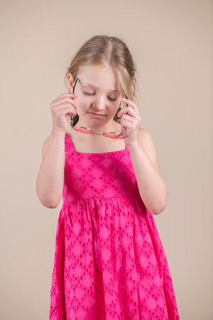Little girl in a pink dress with glasses on a beige backgroundの写真素材
