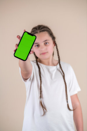 Teenage girl with braids showing smartphone with green screen on beige backgroundの写真素材